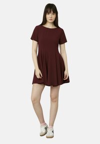 Robe courte bordeaux à manches courtes, avec un col rond et une jupe froncée. Tissu lisse avec un corsage ajusté et un bas fluide, associé à des baskets.