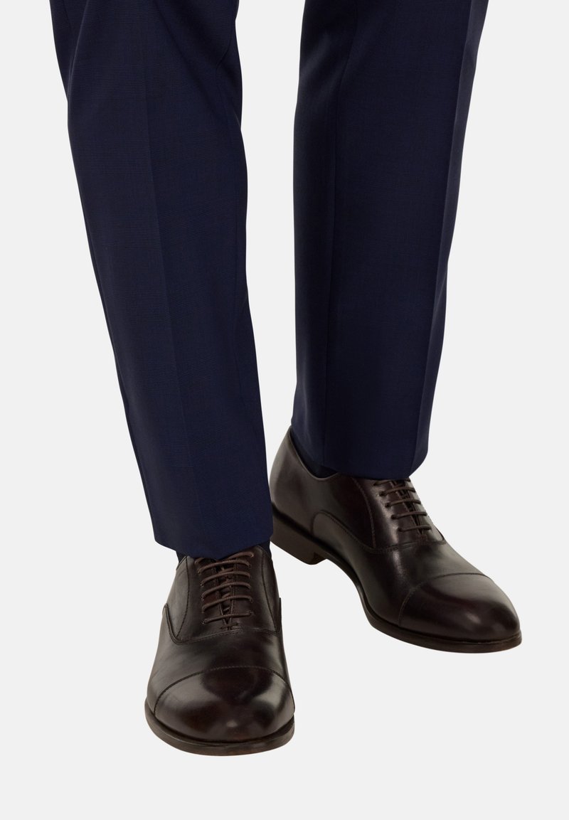 Scarpe da dress in pelle marrone scuro con finitura liscia, con punta arrotondata, design con lacci e leggero tacco, indossate con pantaloni blu navy.