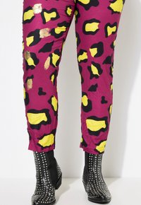 Magenta broek met zwart en gele luipaardvlekken, met een gekreukt textuur. Zwarte studs enkellaarsjes accentueren de outfit.
