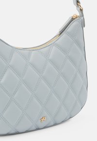 Sac à main en cuir matelassé bleu clair avec une fermeture éclair dorée et un petit logo doré près du coin inférieur, avec une seule bandoulière.