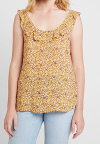 Gul blommig tanktop med volangkrage, med rosa och vita blommönster. Mjukt tyg, avslappnad passform, fållen är lätt rundad.