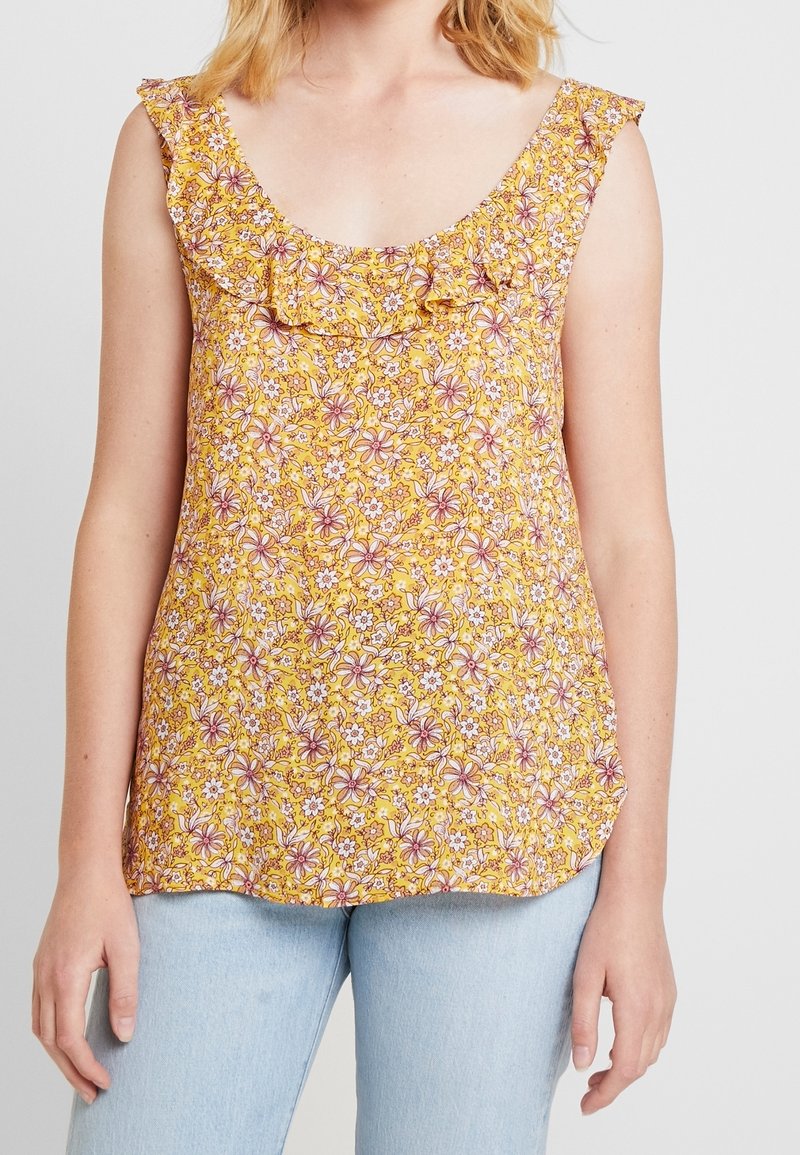 Gul blommig tanktop med volangkrage, med rosa och vita blommönster. Mjukt tyg, avslappnad passform, fållen är lätt rundad.