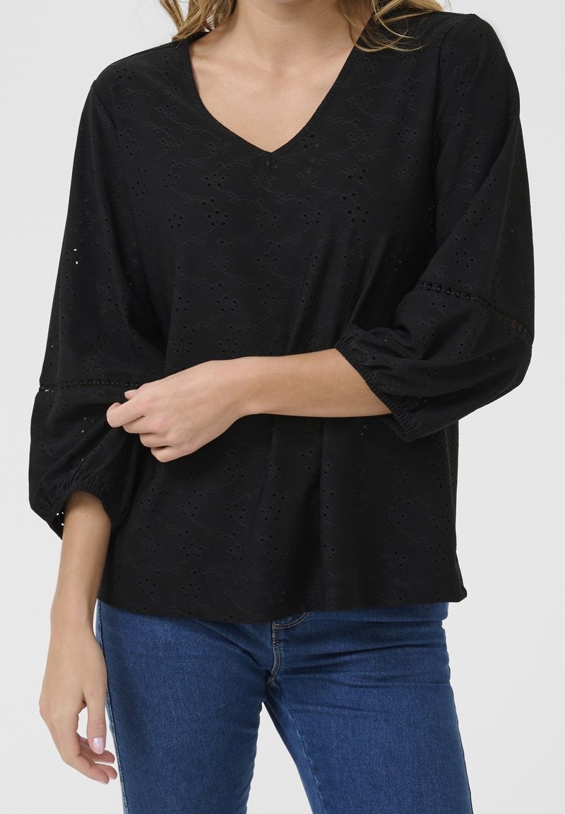 Blouse noire à col en V, avec un motif brodé complexe et des manches bouffantes. Confectionnée dans un tissu léger, avec des poignets élastiqués froncés.