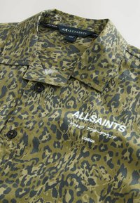 Raglan trumpa rankovėmis kamufliažo žalia spalva su leopardų raštu, su mygtukų užsegimu priekyje ir juodu logotipo akcentu. Minkšta, lengva medžiaga.
