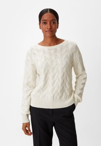 Pull en tricot torsadé crème avec un col rond et des poignets côtelés. Texture douce, coupe ample et motif zigzag bien marqué sur l'ensemble.