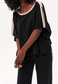 Haut ample noir à manches courtes, avec un accent rose pâle le long de l'encolure et sur le côté. Le matériau semble lisse et léger.