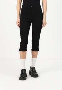 Svarta jeans i cropped-modell tillverkade av ett stretchmaterial. Har en framknapplist, slim fit och något utsvängd nederkant. Bärs med svarta loafers.