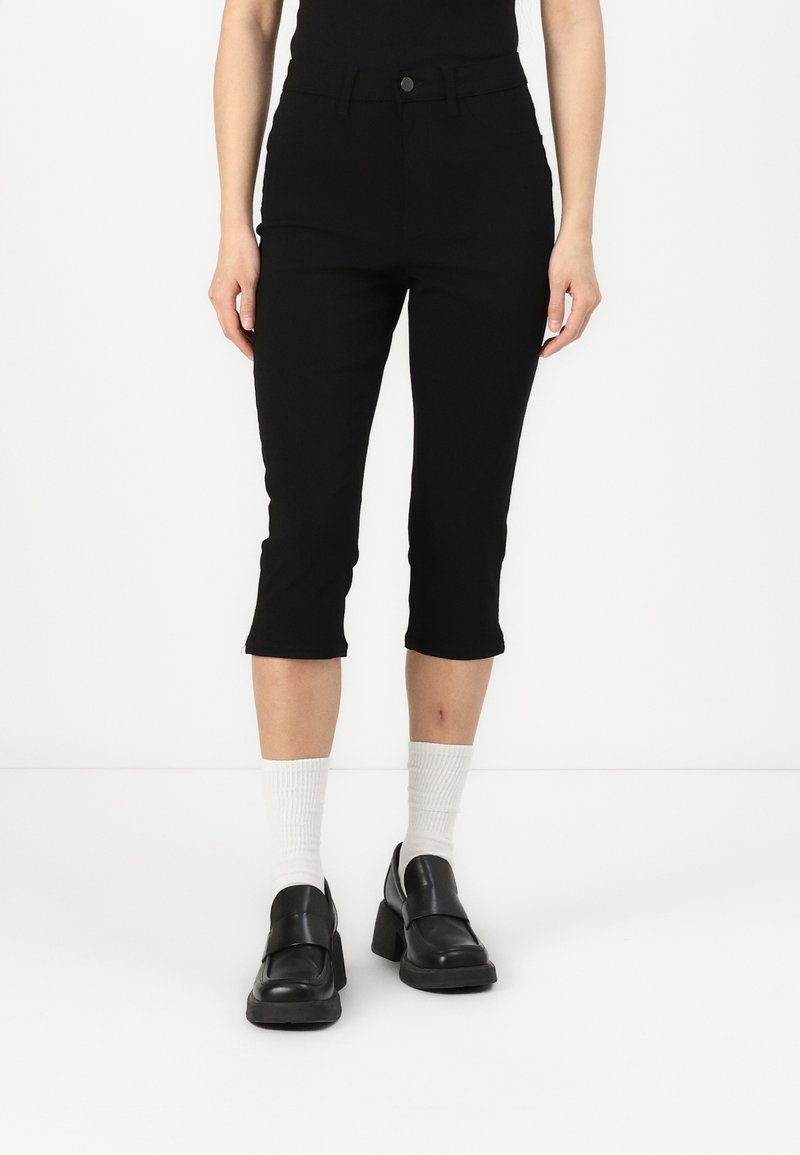 Svarta jeans i cropped-modell tillverkade av ett stretchmaterial. Har en framknapplist, slim fit och något utsvängd nederkant. Bärs med svarta loafers.