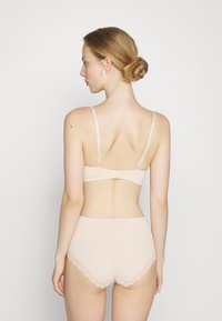 Light pink bra and high-waisted underwear set featuring thin straps and lace trim. Smooth fabric with a fitted design. Seen from the back.