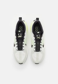 Šedé a bílé tenisky s černými akcenty, texturovaný síťovaný svršek, zelené detaily a černé tkaničky; logo na jazyku a na boku.