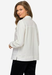 Camicia bianca a maniche lunghe con colletto, fessure laterali e una vestibilità rilassata, realizzata in un materiale morbido e liscio.
