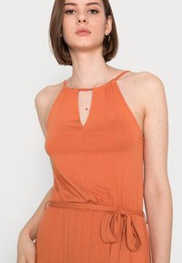 Vestido laranja com decote halter, frente com abertura em forma de olho, tecido franzido na gola e cinto atado na cintura. Textura suave.