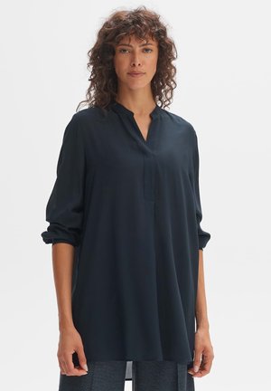 Blouse bleu foncé avec une coupe décontractée, manches longues retroussées aux poignets, décolleté en forme de clé et texture de tissu lisse et douce.