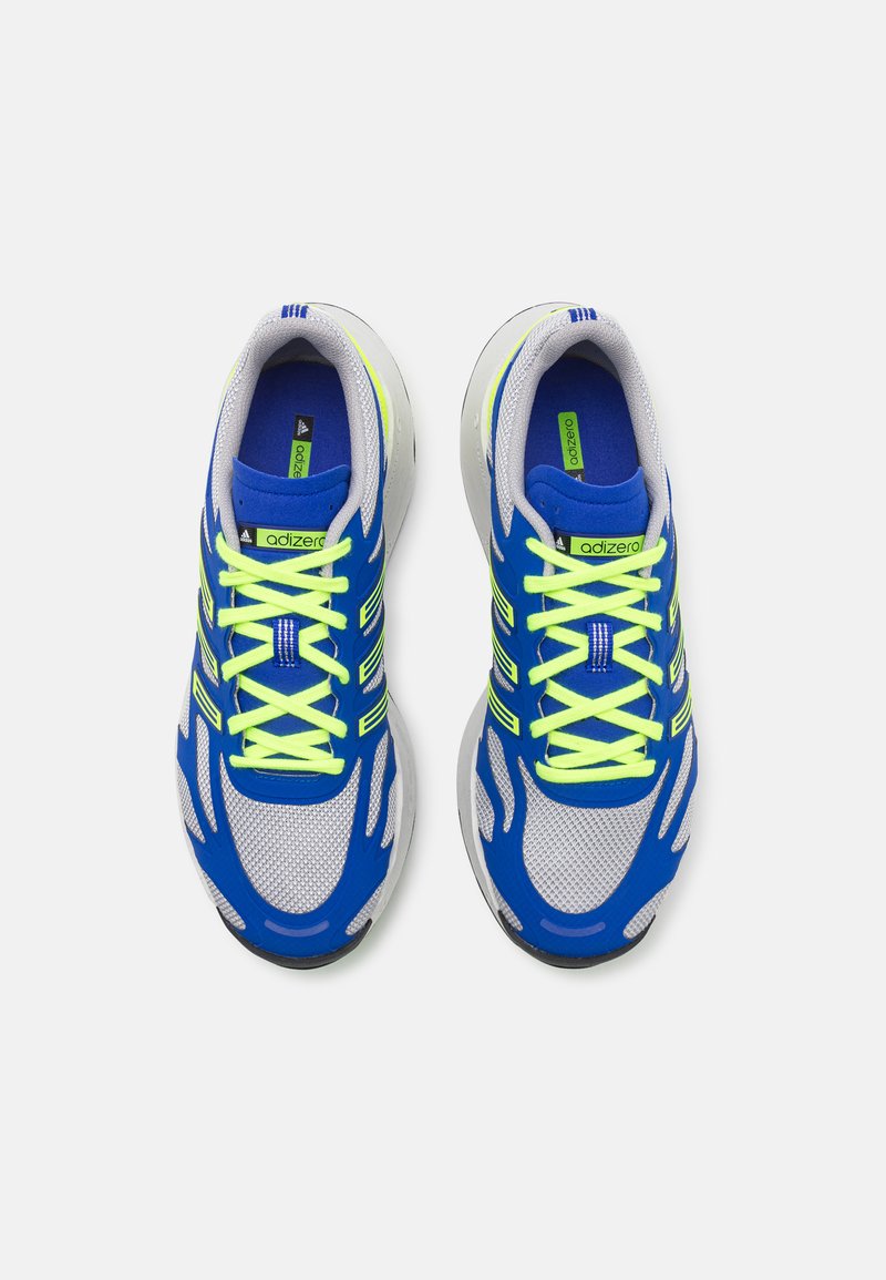 Scarpe da ginnastica blu e grigie con tomaia in rete, lacci gialli brillanti e dettagli testurizzati lungo i lati e la punta.