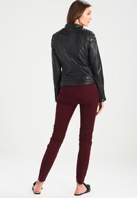 Sort læder motorcykeljakke med quiltede skulderdetaljer, parret med slim-fit bordeaux bukser og åbentåede sorte sandaler.
