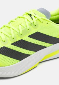 Neon yellow athletic shoe with black Adidas stripes, mesh upper, textured finish, and a padded grey collar; features a white sole with yellow accents.