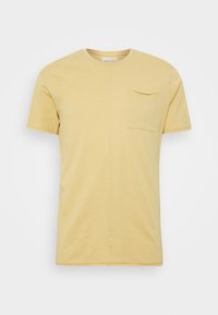 Beżowa męska koszulka z krótkim rękawem, z okrągłym dekoltem i małą kieszonką na lewej stronie.