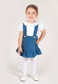 Niebieska sukienka na szelkach z dwoma guzikami i falbaną przy dole. W zestawie z białą bluzką i białymi rajstopami.
