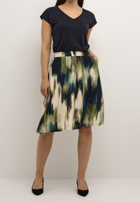 Top en v bleu marine associé à une jupe multicolore longueur genoux avec des motifs abstraits en vert, bleu et crème. La jupe comprend des poches.