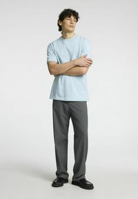 Šviesiai mėlyna medvilninė marškinėliai su tamsiai pilkomis struktūrinėmis kelnėmis ir juodais loaferiais, pasižymintys laisvu siluetu ir apvaliu kaklu.