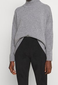 Grijze gebreide coltrui met een relaxte fit, geribbelde kraag en zoom, zijsplitten, gecombineerd met zwarte broek. Zachte textuur en oversized ontwerp.