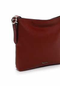 Borsa a tracolla in pelle rossa con una texture morbida, forma arrotondata e dettaglio in metallo argentato. Logo del marchio delicatamente impresso sulla parte anteriore.