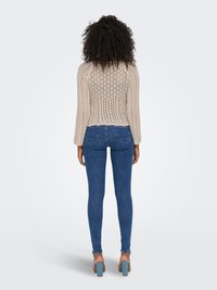 Bež pleteni pulover s teksturiranim uzorkom, dugim rukavima i skraćenim dizajnom, uparen s prilagođenim plavim trapericama i svijetloplavim potpeticama.