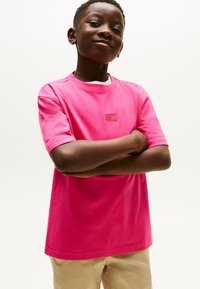 Jasnoróżowa koszulka z krótkim rękawem wykonana z bawełny, z małą, strukturalną naszywką logo z przodu. Gładki materiał w klasycznym kroju.