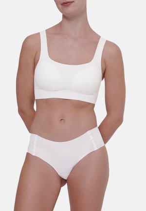 Donna che indossa un reggiseno senza cuciture bianco e mutandine bianche a vita alta abbinate, in piedi con le mani dietro la schiena.