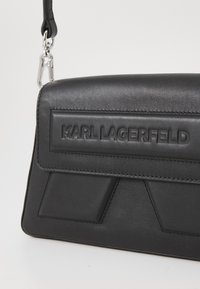 Black leather handbag with embossed logo and geometric accents. Features a structured shape, silver hardware, and a detachable strap.