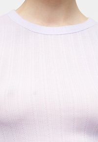 Gros plan d'une personne portant un haut en maille côtelée lavande clair avec un col rond et un motif vertical subtil.