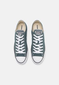 Zelene platnene nizke superge z belimi čipkami, gumijastim pokrovom za prste in črnimi robovi. Imajo klasičen dizajn s oznako "Converse All Star".