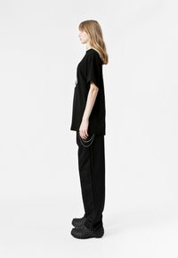 Camiseta negra de gran tamaño con estampado gráfico, combinada con pantalones negros holgados con un acento de cadena y calzado negro texturizado.