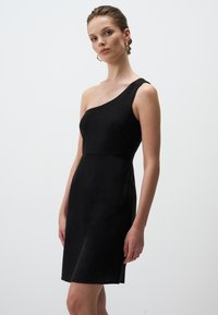 Schulterfreies schwarzes Kleid, figurbetonte Passform, Mid-Thigh-Länge, strukturiertes Gewebe, subtiler Glanz und keine sichtbaren Verschlüsse oder Muster.