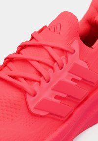 Chaussure de sport rose vif avec une tige texturée, des lacets plats et trois bandes proéminentes sur le côté. Semelle en caoutchouc légère.