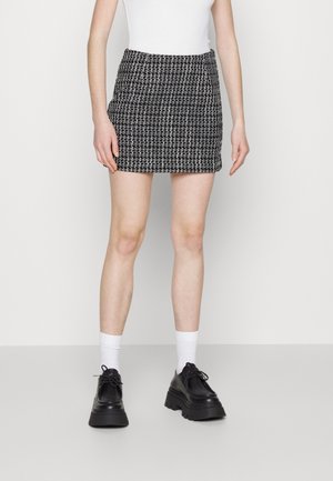 Gonna mini a scacchi bianco e nero con un design aderente, tessuto testurizzato e una vita elastica, indossata con calze bianche e scarpe nere chunky.