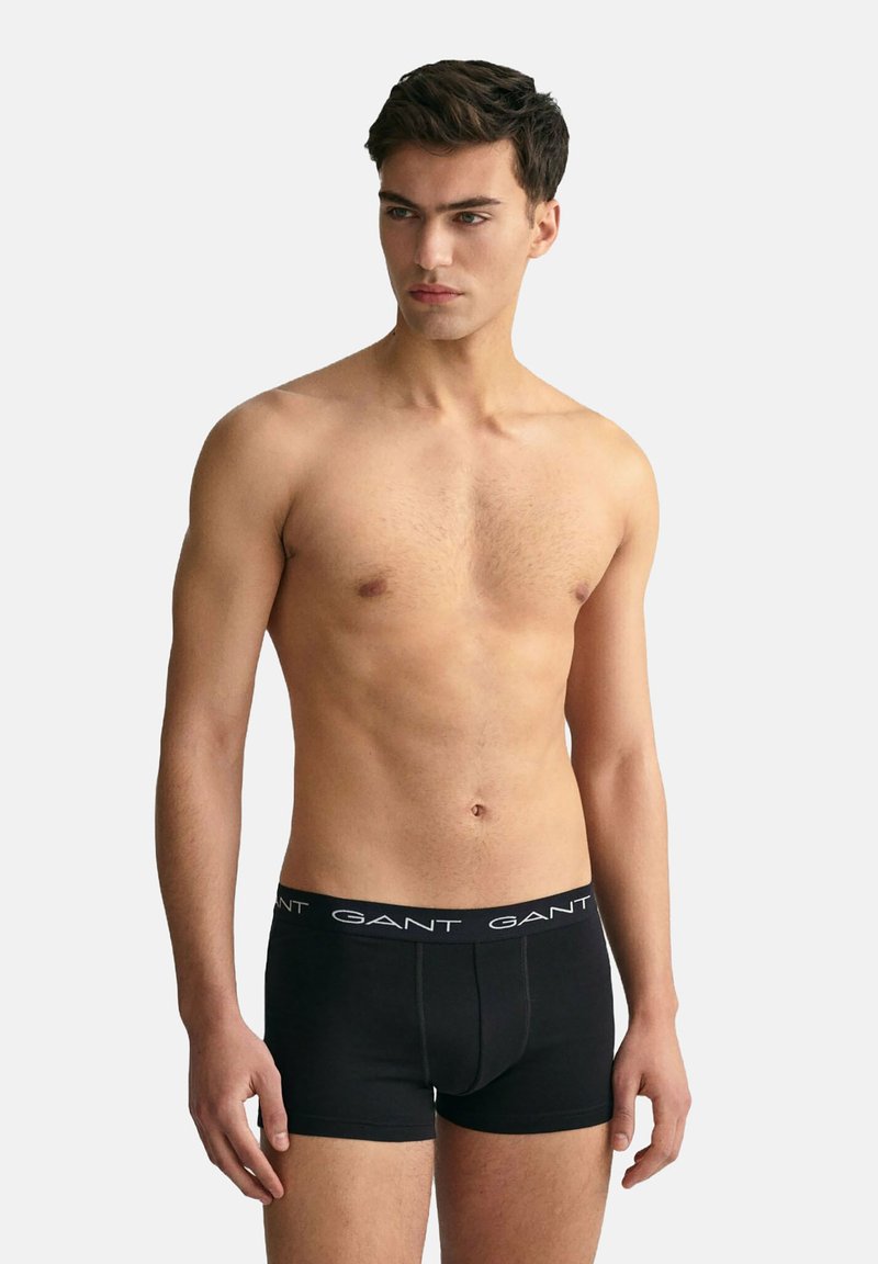 Black cotton boxer briefs with a logo waistband, fitted design, and smooth texture, displayed on a male model against a neutral background.