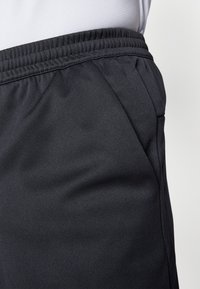 Lähivõte mustast elastse vöökoht ja tasku detail casual pükstel, millele on kantud valge tekstureeritud topp.