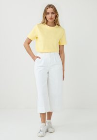 T-shirt di cotone gialla, maniche corte, abbinata a pantaloni bianchi a gamba larga e sneakers bianche. Outfit semplice e informale con una vestibilità comoda.