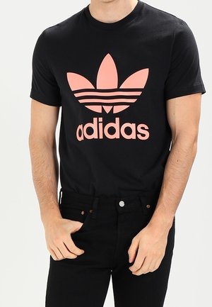 Czarny bawełniany T-shirt z dużym różowym logo Adidas trefoil z trzema poziomymi paskami, zestawiony z czarnymi dżinsami.