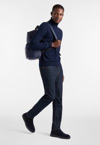 Mornarsko pleten turtleneck, temno modri kavbojki in mornarske semiš čevlji; nosi usnjeni nahrbtnik v enaki barvi s številnimi predelki.