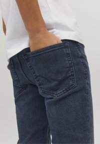 Vaqueros azul oscuro con corte recto, que presentan detalles en la costura de los bolsillos traseros y una cintura ajustada. Se puede apreciar una textura de denim suave.