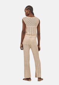 Conjunto de dos piezas de punto en beige claro. Top sin mangas con textura de patrón, combinado con pantalones acampanados que presentan un diseño similar y aberturas laterales.