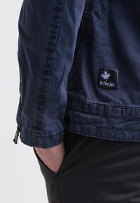 Marinblå jacka i lättviktsmaterial med dragkedja och en patch-logotyp. Ärmen har en slät yta och en skräddarsydd passform.