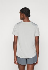 T-shirt de sport gris clair à manches courtes avec un motif en maille texturée et des manches raglan, porté avec un short gris foncé.