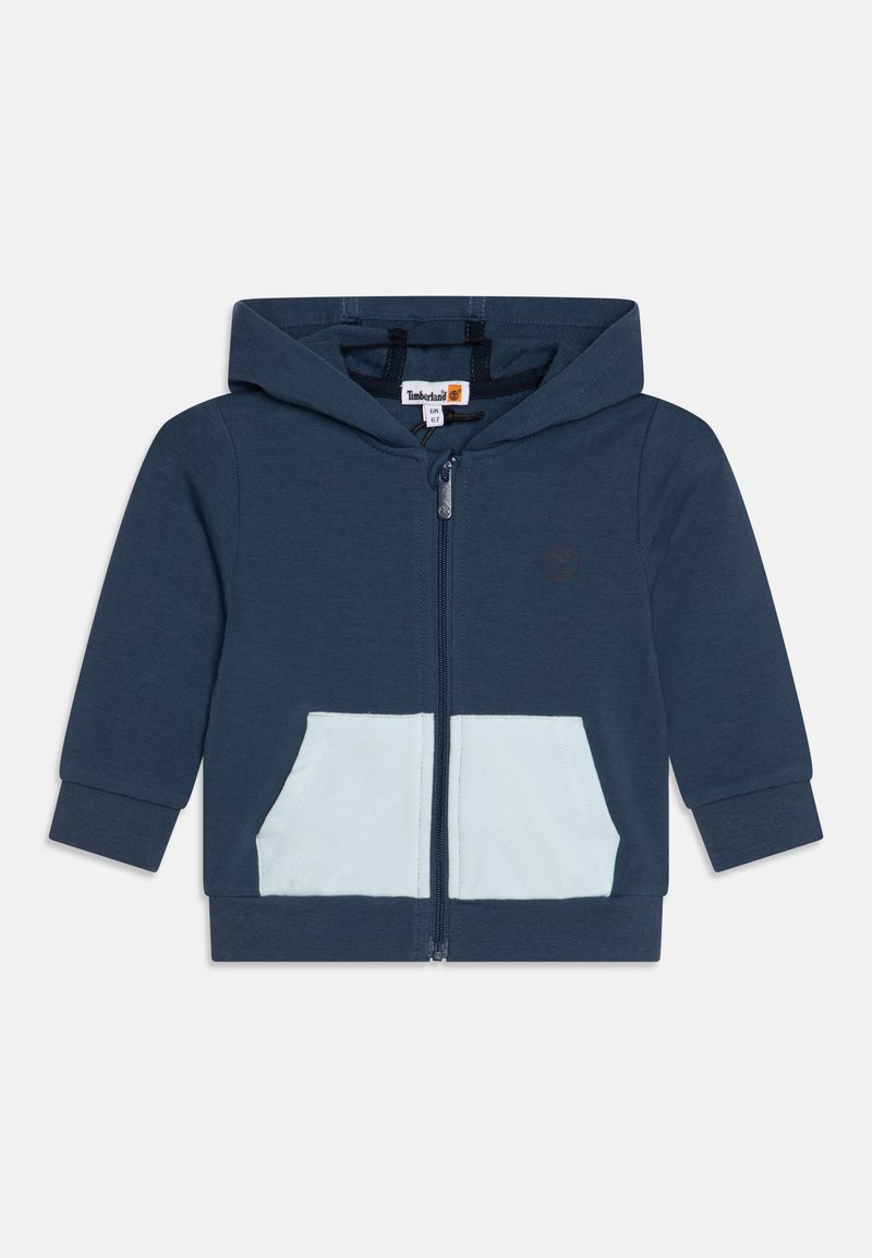 Felpa zip-up color navy con tasca azzurro chiaro. Presenta una texture morbida e un cappuccio con cordino. Logo Timberland sul petto.