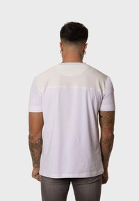 Camiseta blanca de manga corta con un panel trasero superior texturizado, tela suave y cuello redondo. Presenta un dobladillo recto y un diseño ajustado.