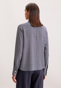 Camicia a maniche lunghe in blu navy con un motivo geometrico bianco. Presenta un collo classico e polsini con bottone, realizzata in tessuto leggero.