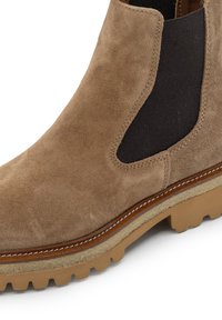 Stivale alla caviglia in suede marrone con pannelli laterali elastici, suola in gomma e cucitura beige in contrasto lungo la parte centrale. Superficie piatta e strutturata.