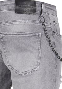 Jasnoszare dżinsy z denimu z czarną skórzaną metką, łańcuszkowym detalem po boku i przetarciami na kieszeniach.